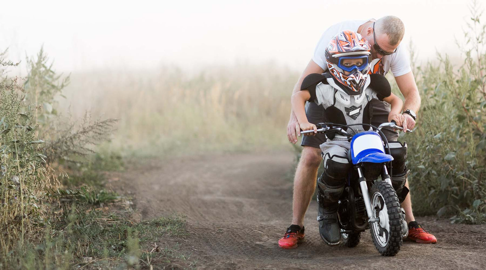 Man teaching a child how to ride a small motorcycle on a dirt path | eMotoX Sports