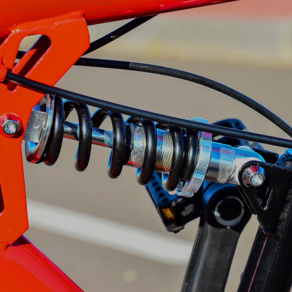 Close-up of rear coil shock suspension on a mountain bike, showing spring, linkage, and frame components during inspection. - eMotoX Sports