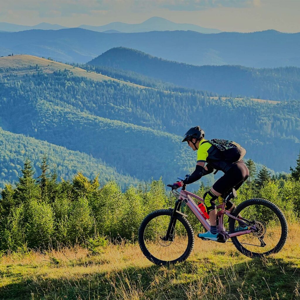 Mountain biker riding along a scenic trail with rolling hills and countryside in the background at eMotoX Sports