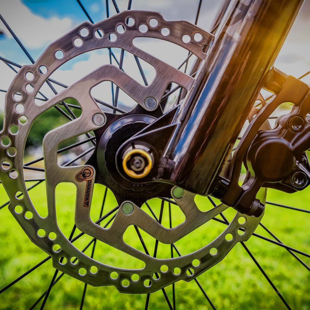 Close-up of bicycle front wheel disc brake front wheels disc rotor and calliper, showing clean braking components and hub assembly - eMotoX Sports