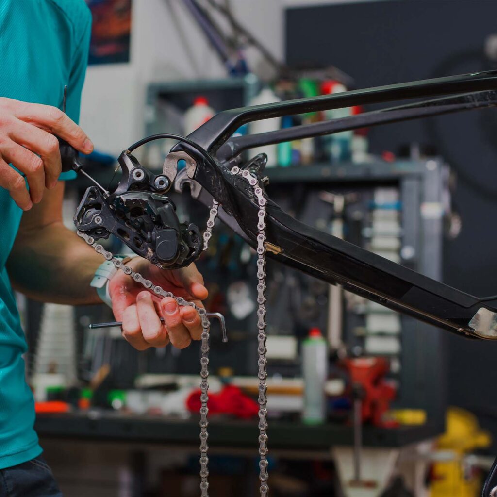 Bicycle mechanic adjusting rear derailleur and chain during bike service. | eMotoX Sports