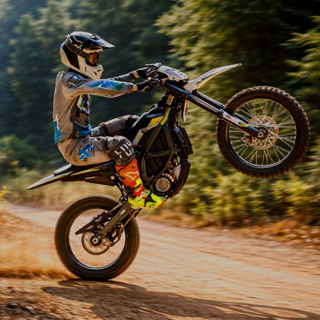 Rider performing a wheelie on an electric motocross bike while riding off-road on a dirt trail. | eMotoX Sports